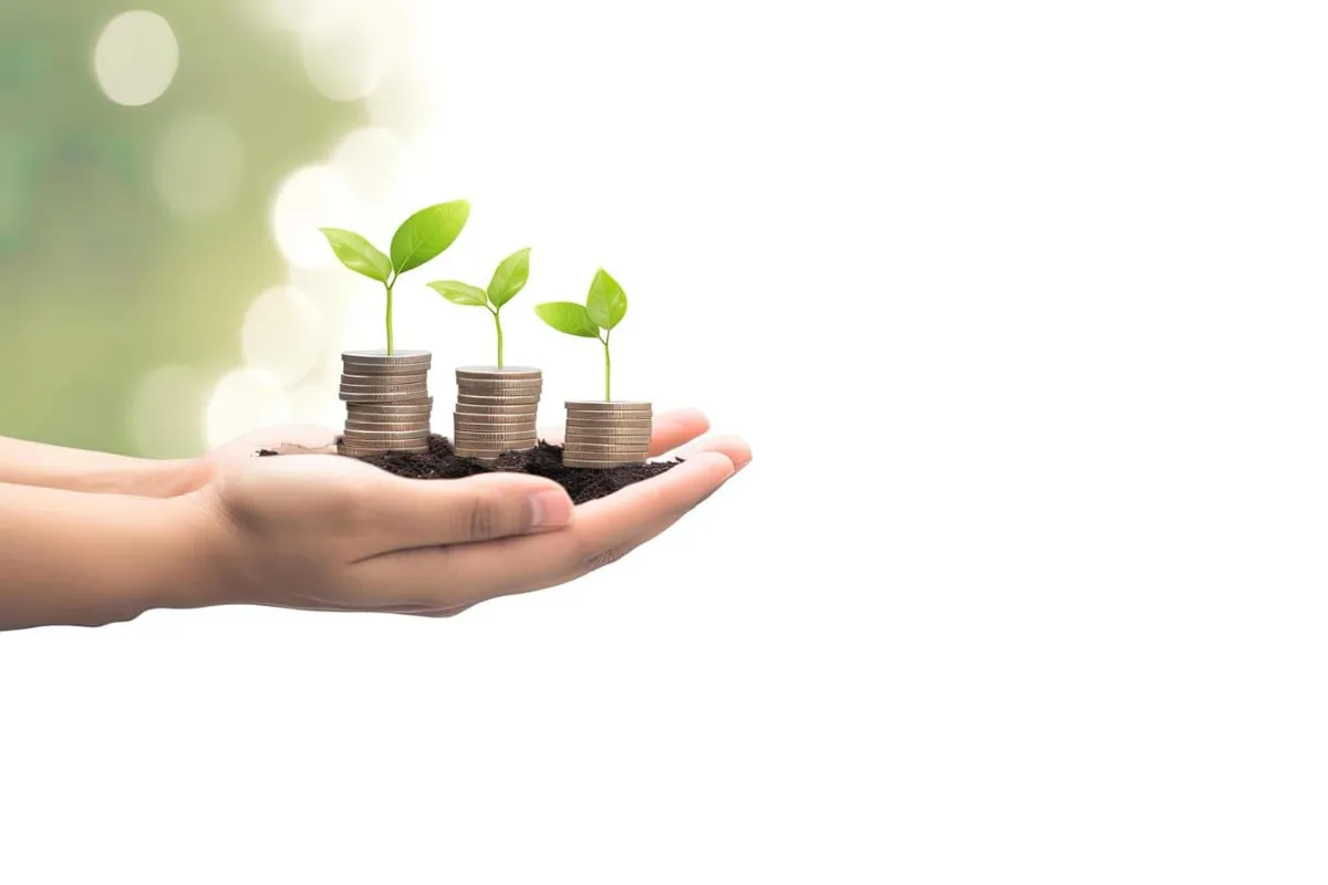 Des mains tenant de la terre d'où poussent des plants sur des pièces de monnaie